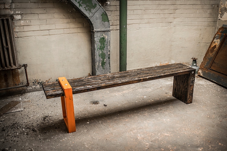 Puede incluir: Un banco de madera r&uacute;stico con un acabado marr&oacute;n oscuro y patas de metal naranja. El banco est&aacute; hecho de madera recuperada y tiene un dise&ntilde;o simple e industrial.
