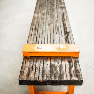 Puede incluir: Un banco de madera largo con un marco de metal naranja brillante. El banco est&aacute; hecho de madera recuperada y tiene un aspecto r&uacute;stico. El marco de metal naranja agrega un toque moderno al banco.