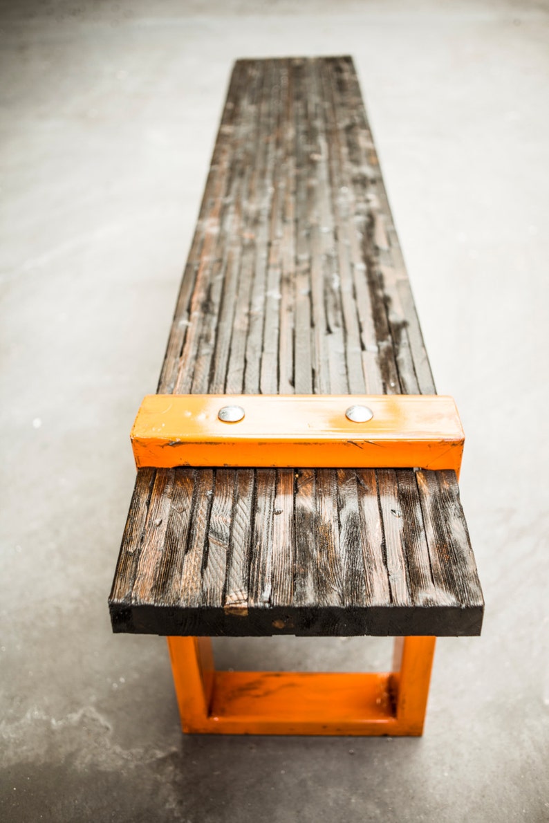 Puede incluir: Un banco de madera largo con un marco de metal naranja brillante. El banco est&aacute; hecho de madera recuperada y tiene un aspecto r&uacute;stico. El marco de metal naranja agrega un toque moderno al banco.
