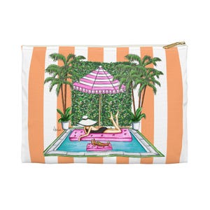 Könnte beinhalten: Eine Reißverschlusstasche mit einer lebendigen Illustration einer Frau, die sich an einem Pool entspannt. Die Tasche hat ein weißes und orangefarbenes Streifenmuster auf der Vorderseite und einen goldenen Reißverschluss. Die Illustration zeigt einen rosa Sonnenschirm, Palmen und eine sonnenbadende Frau.