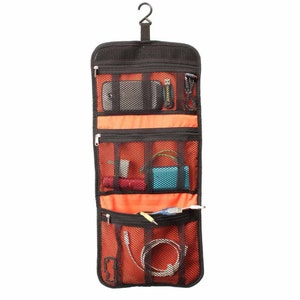 May include: A black hanging travel organiser with multiple zippered compartments and mesh pockets. The organiser is filled with various items, including a phone, cords, and a small blue case.