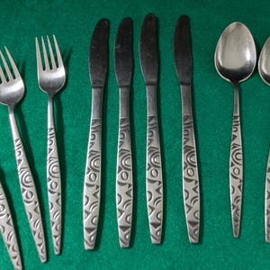 May include: A set of stainless steel flatware consisting of four forks, four knives, and five spoons. Each piece features a distinct geometric pattern of circles and triangles embossed along the handle, providing a consistent design across the set.