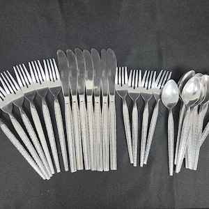 May include: A stainless steel flatware set consisting of five dinner forks, six dinner knives, four salad forks, and six spoons. Each piece features a textured, decorative pattern along the handle, providing a consistent look across the collection.