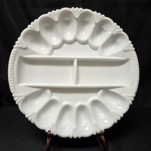 May include: A circular white milk glass serving platter featuring twelve individual oval-shaped indentations arranged around the perimeter and a central rectangular divided section with two compartments, finished with a beaded edge detail.