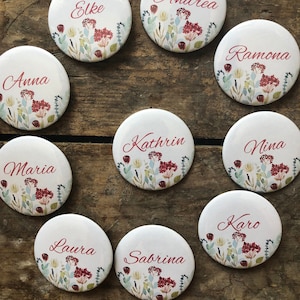 Op de afbeelding: Tien ronde witte plaatskaarten met bloemmotieven en rode namen, waaronder Anna, Andrea, Elke, Sabrina, Maria, Laura, Kathrin, Karo, Ramona en Nina.