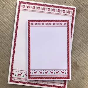 Pode incluir: Dois blocos de notas brancos com bordas de padrões vermelhos e brancos. O bloco de notas maior tem um padrão de flocos de neve vermelhos e brancos. O bloco de notas menor tem um padrão de renas vermelhas e brancas.