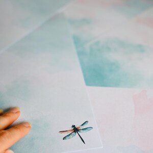 Peut inclure: Une pile de papier &agrave; lettres blanc avec un motif aquarelle de nuages bleus et roses. Une libellule est imprim&eacute;e sur la feuille de papier sup&eacute;rieure.