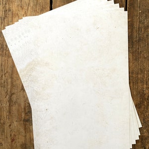 May include: A stack of white paper sheets with a slightly textured surface, lying on a wooden surface.
