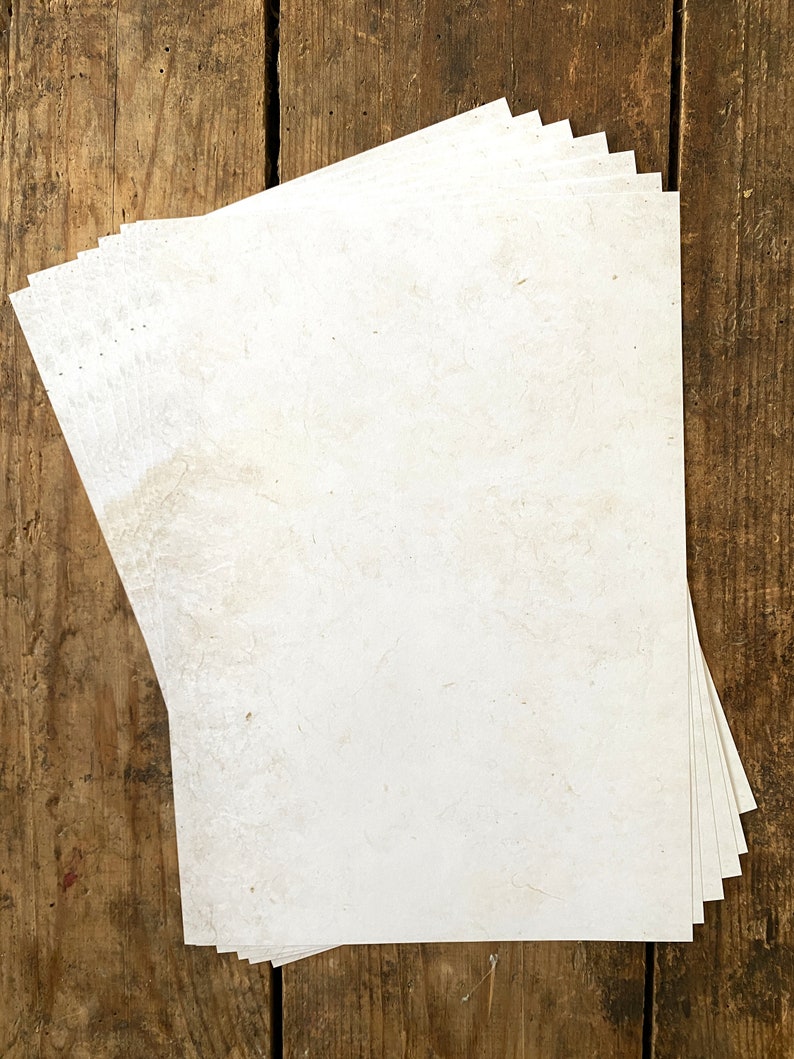 May include: A stack of white paper sheets with a slightly textured surface, lying on a wooden surface.