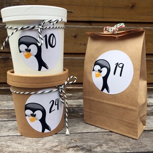 May include: Three brown paper containers with penguin stickers. The containers are decorated with twine and have numbers 10, 19, and 24 on them.