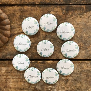 May include: Ten round white badges with green foliage designs and names printed in black. The names are: Alina, Anja, Claudia, Jessica, Loreen, Manja, Tina, Jasmin, Isabel.