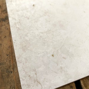 May include: A close-up of a white textured paper surface with subtle brown and gray marbling. The paper has a slightly rough texture.