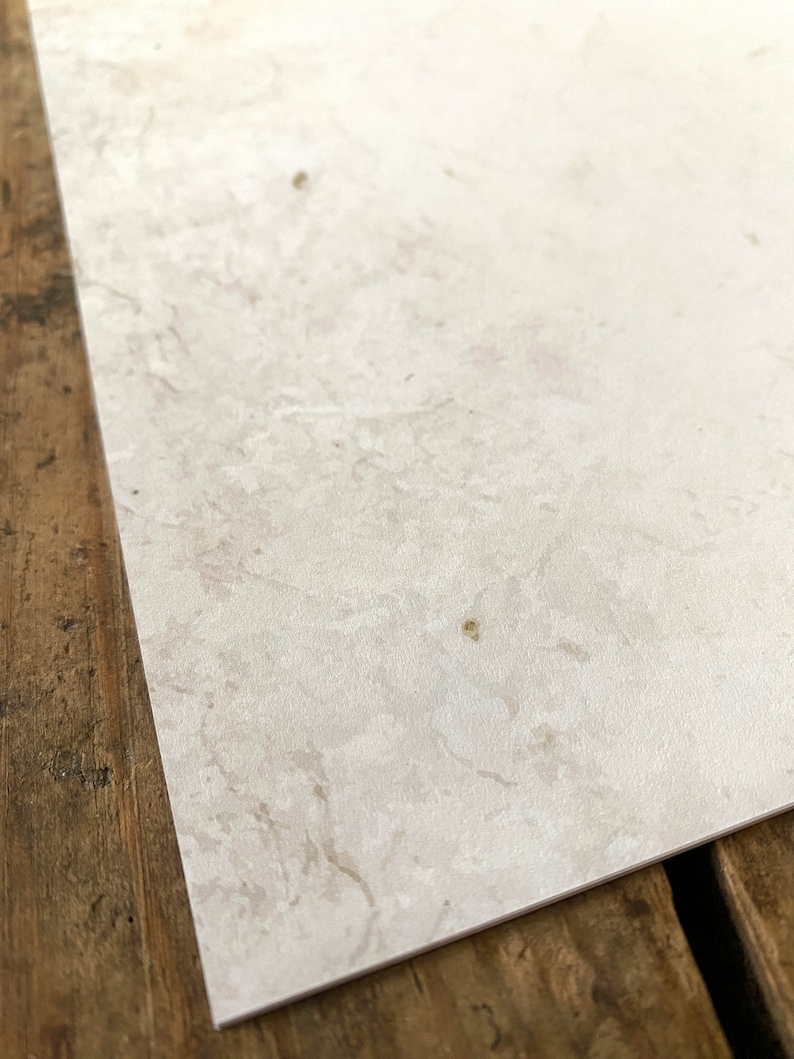 May include: A close-up of a white textured paper surface with subtle brown and gray marbling. The paper has a slightly rough texture.