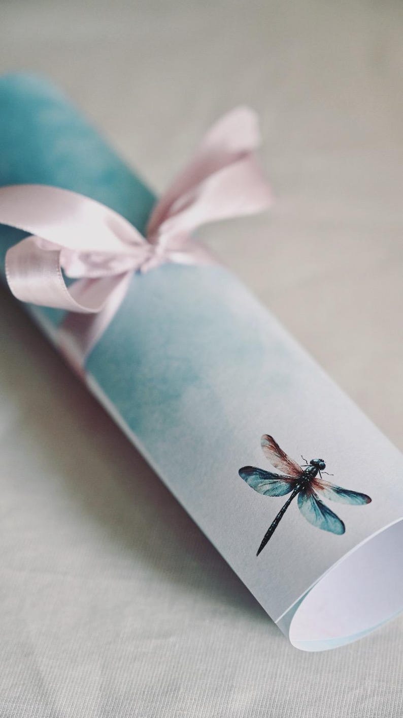 Peut inclure: Une impression enroul&eacute;e avec un fond aquarelle bleu clair et un ruban rose nou&eacute; autour. Une libellule est imprim&eacute;e sur le devant de l'impression.