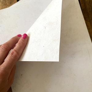 May include: A stack of white paper with a slightly textured surface. The paper is being lifted to reveal the layers underneath.