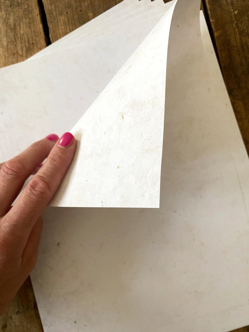 May include: A stack of white paper with a slightly textured surface. The paper is being lifted to reveal the layers underneath.