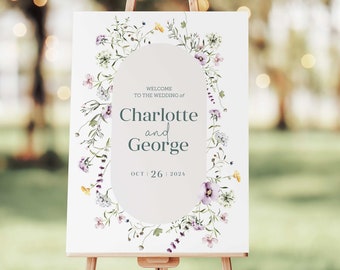 May include: A white wedding welcome sign with a floral wreath border. The sign reads "Welcome to the wedding of Charlotte and George Oct 26 2024".