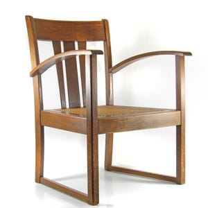 May include: A wooden armchair with a woven seat and curved armrests. The chair has a dark brown finish and a rectangular back with vertical slats. The design is simple and classic, suitable for various interior styles.