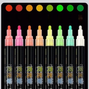 Op de afbeelding: Een set van acht markers met zwarte behuizing en gekleurde doppen, voorzien van Chinese karakters op de labels. Boven elke marker staat een bijbehorende gekleurde stip, variërend van rood en oranje tot geel, limoen, groen, blauwgroen en wit.