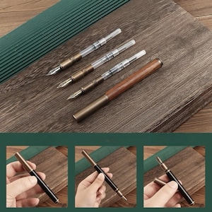May include: A collection of fountain pens with brass and wood accents. The pens have clear ink reservoirs and ornate nibs. One pen is fully assembled, while others are disassembled. The pens are displayed on a wooden surface with a green textured background.