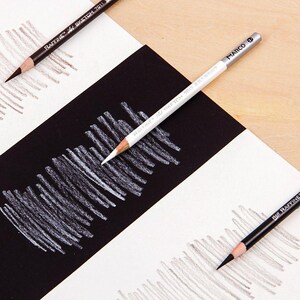 May include: Close-up of three drawing pencils on a white and black striped surface. The pencils are labelled "RAFINE" and "MARCO".