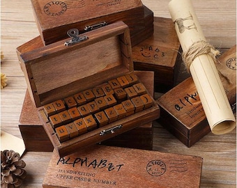May include: Wooden box with a set of alphabet stamps. The stamps are arranged in a grid and are made of wood. The box is brown and has a vintage look. The box is labeled "STAMP ALPHABET" and "HANDWRITING UPPER CASE & NUMBER".