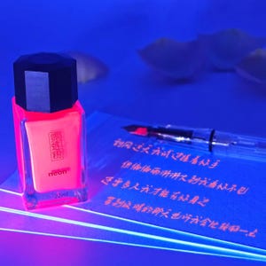 May include: A neon pink nail polish bottle with a black cap, labeled "neon" and "22ml". A clear fountain pen and a blue notepad with Chinese characters are also visible.
