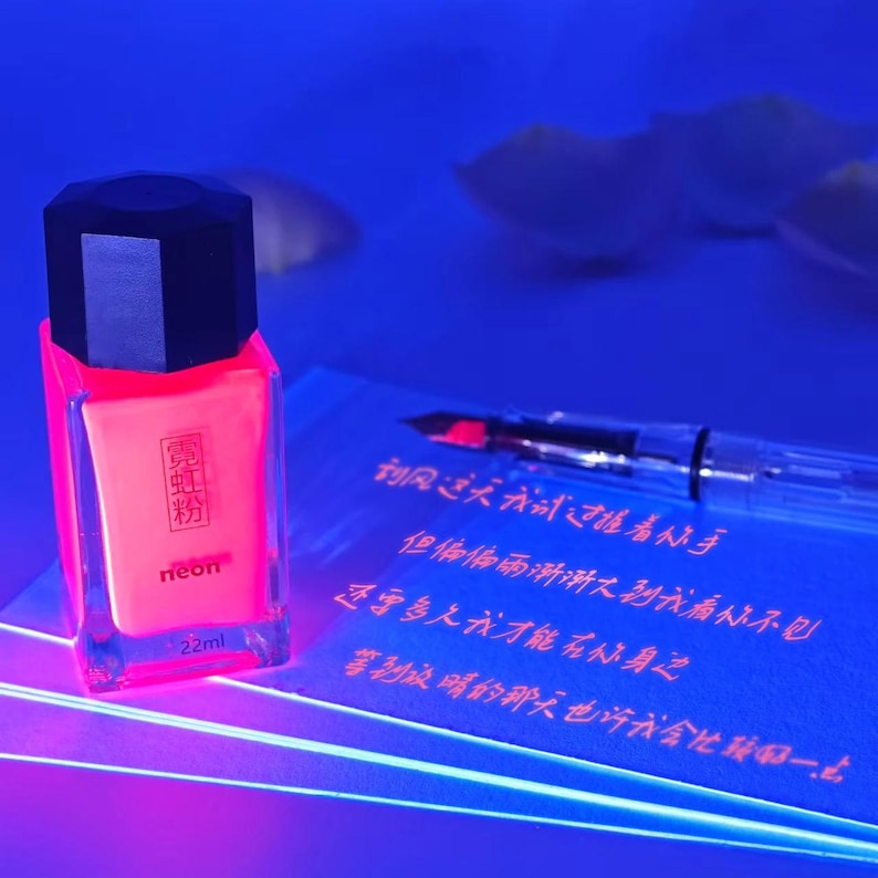 May include: A neon pink nail polish bottle with a black cap, labeled "neon" and "22ml". A clear fountain pen and a blue notepad with Chinese characters are also visible.