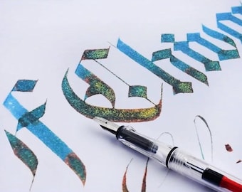 May include: A clear fountain pen with a silver nib rests on white paper featuring hand-lettered calligraphy in a gothic script. The ink displays a gradient of shimmering blue, green, and gold tones, creating a textured and metallic appearance.