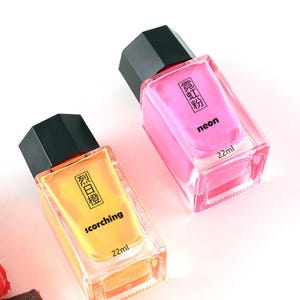 May include: Two glass perfume bottles with black caps. One bottle contains a neon pink liquid with the word "neon" printed on the front. The other bottle contains a yellow liquid with the word "scorching" printed on the front. Each bottle is labeled with "22ml".