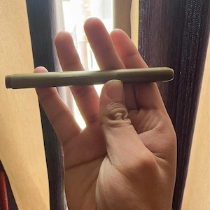 Puede incluir: Un bol&iacute;grafo de color lat&oacute;n de estilo vintage con un dise&ntilde;o de cuerpo acanalado. El bol&iacute;grafo se sostiene en una mano, mostrando su forma cil&iacute;ndrica y delgada. La tapa del bol&iacute;grafo es visible, y la est&eacute;tica general sugiere un instrumento de escritura cl&aacute;sico.