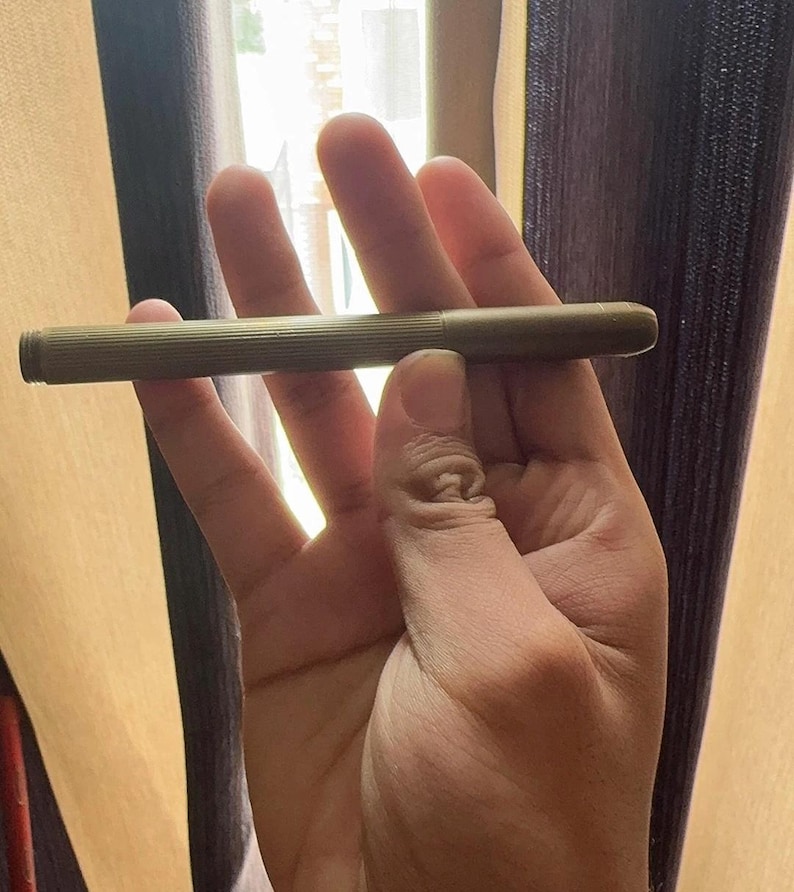 Puede incluir: Un bol&iacute;grafo de color lat&oacute;n de estilo vintage con un dise&ntilde;o de cuerpo acanalado. El bol&iacute;grafo se sostiene en una mano, mostrando su forma cil&iacute;ndrica y delgada. La tapa del bol&iacute;grafo es visible, y la est&eacute;tica general sugiere un instrumento de escritura cl&aacute;sico.