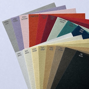 May include: A fan-shaped collection of textured paper sheets in various colors including Smoke Gray, Star Cloud, Peach Blossom, Terracotta, Festive Red, Brick Red, Seafoam Green, Jade Green, Deep Blue, Ivory White, Mist White, Cloud Cream, Soft Honey, Sand Beige, Tea Brown, Frost Gray, and Ink Black.