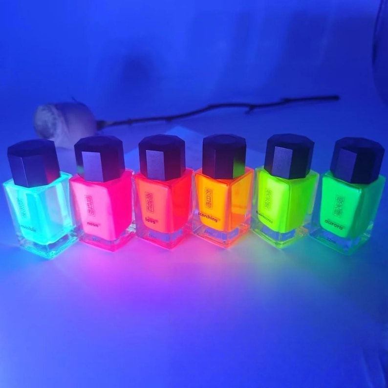 May include: Six neon-colored nail polish bottles with black caps are arranged in a row. The colors include light blue, pink, orange, yellow, and green. Each bottle has a square base and a rectangular label.