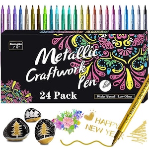 Op de afbeelding: Een set van 24 metallic craftwork pennen in diverse kleuren, weergegeven boven een zwarte doos met de tekst "Metallic Craftwork Pen 24 Pack". De afbeelding toont ook beschilderde stenen en de woorden "Happy New Year".