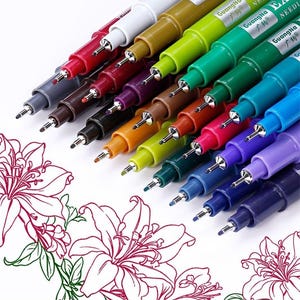 May include: A collection of colorful fine-tip pens, each with a metal tip, arranged diagonally. The pens are in various colors, including red, green, blue, and purple. The text "GuangNa" is visible on the pens. Floral line art is in the foreground.