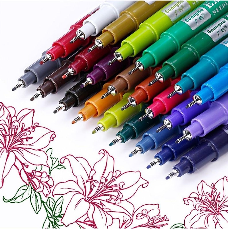 May include: A collection of colorful fine-tip pens, each with a metal tip, arranged diagonally. The pens are in various colors, including red, green, blue, and purple. The text "GuangNa" is visible on the pens. Floral line art is in the foreground.