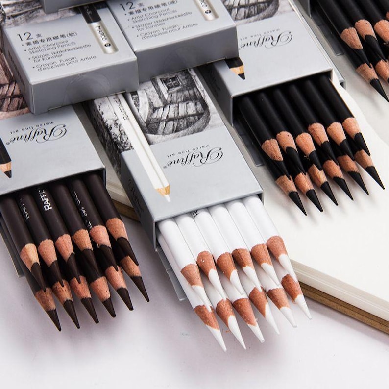 May include: A set of 12 black and white drawing pencils in a silver box with the brand name "Raffine" printed on the box. The pencils are arranged in two rows, with the black pencils on the top row and the white pencils on the bottom row. The pencils are sharpened and ready to use.