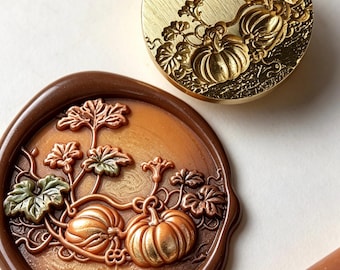 May include: A circular brass wax seal stamp featuring an engraved pumpkin vine design, paired with a matching brown wax seal impression showing two pumpkins and leaves, and a single brown wax stick positioned in the lower right corner.