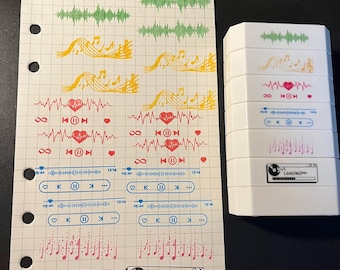 May include: A sheet of grid paper featuring various music-themed stickers including green sound waves, yellow musical notes, red heartbeats, blue playback controls, and black loading bars, alongside a stack of six white rectangular stamp blocks.