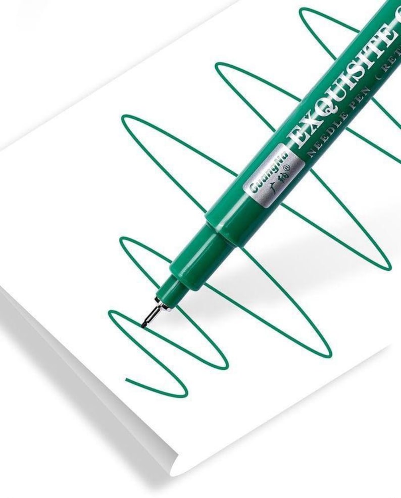 May include: A green needle pen labeled "EXQUISITE" is shown drawing a green, curved line on white paper. The pen has a silver tip and a dark green barrel. The paper is white and slightly angled.