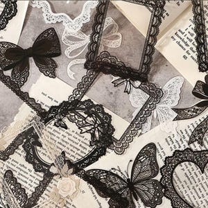 May include: A collection of black and white lace-style stickers featuring intricate frames, bows, and butterfly shapes. The designs include rectangular, circular, and heart-shaped borders with detailed patterns, layered over pages of vintage printed text.