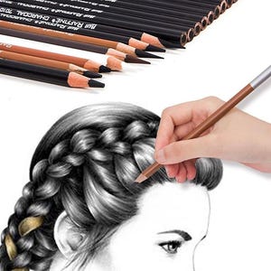 May include: A set of 12 charcoal pencils in a black box with the text "MUR RAFFINE CHARCOAL" on the side. The pencils are being used to draw a portrait of a woman with braided hair.