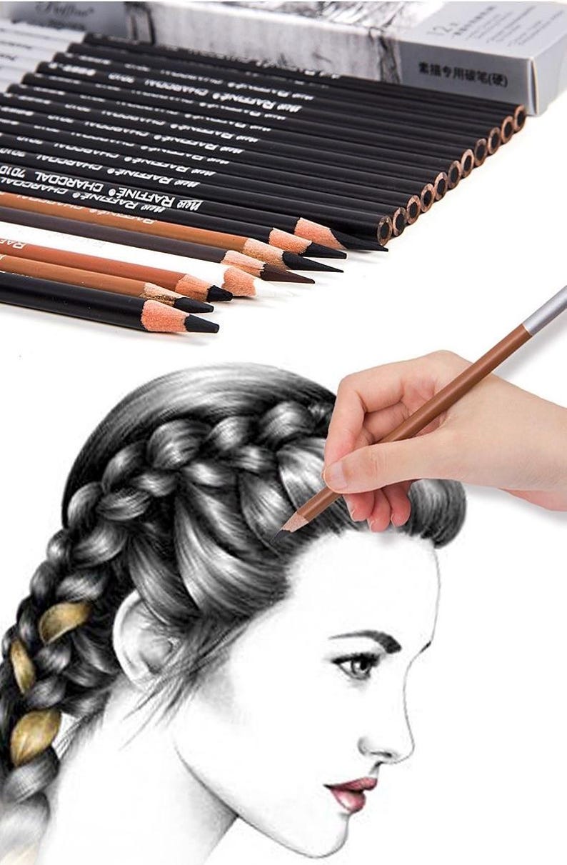 May include: A set of 12 charcoal pencils in a black box with the text "MUR RAFFINE CHARCOAL" on the side. The pencils are being used to draw a portrait of a woman with braided hair.