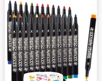 May include: A set of black fabric markers with colored caps and tips, each labeled "FABRIC MARKER" in white text. The markers are arranged in rows behind a small white zippered pouch decorated with colorful drawings of a dog, duck, and frog.