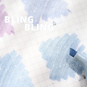 May include: Close-up of a light blue highlighter pen with a blue tip, creating a sparkling effect on a grid paper. The word "BLING" is written in white. The background features light blue and purple glittery brushstrokes.