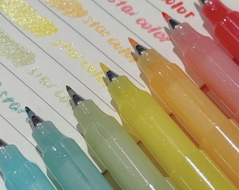 May include: A set of six glitter gel pens in shades of red, orange, yellow, light green, light blue, and pink. Each pen features a translucent barrel and a matching colored ink swatch on paper with the printed text Star color visible.