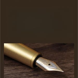 Puede incluir: Primer plano de una pluma estilogr&aacute;fica dorada con plum&iacute;n plateado. La pluma se encuentra sobre una superficie de madera marr&oacute;n oscuro. El texto "RETRO FOREST" est&aacute; en la parte superior.