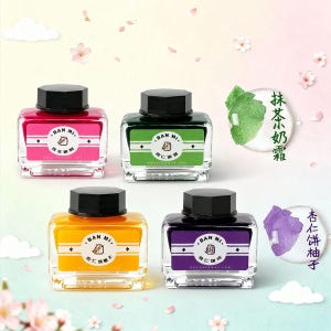 May include: Four glass ink bottles with black lids, each with a different coloured label: pink, green, yellow, and purple. Each label has the text "BAN MI" and a small illustration. Two small illustrations of matcha and almond cakes are also present.