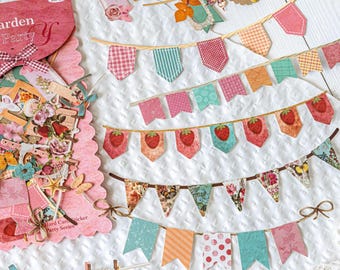May include: A set of decorative paper bunting and stickers labeled Garden Party, featuring various pennant shapes with patterns including strawberries, floral prints, gingham, and polka dots, suspended on thin twine strings.